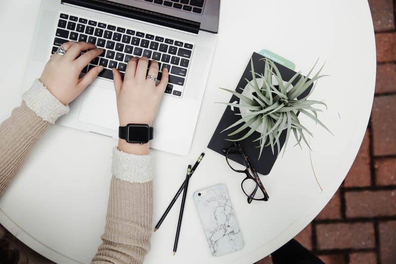 Flat lay of someone typing on a laptop, with a phone, glasses, pencils and plant 