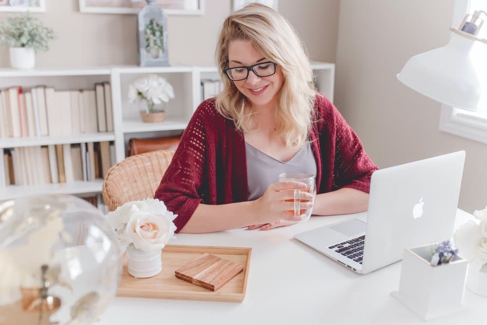 A virtual marketing assistant with blonde hair and glasses sat at her laptop holding a mug and smiling