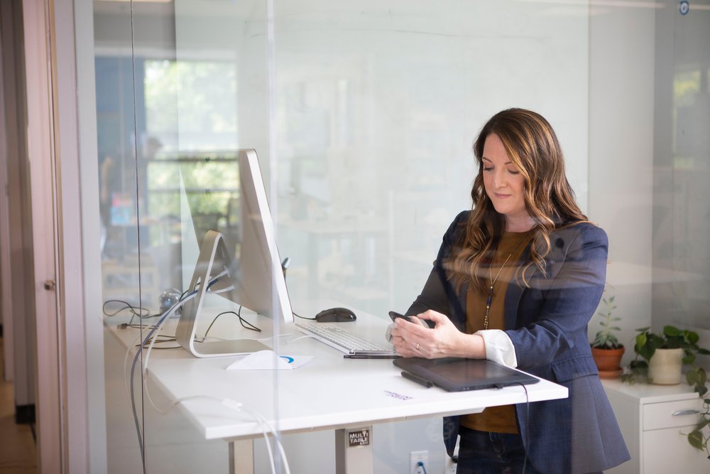 woman with brown hair at a standing desk looking at her phone