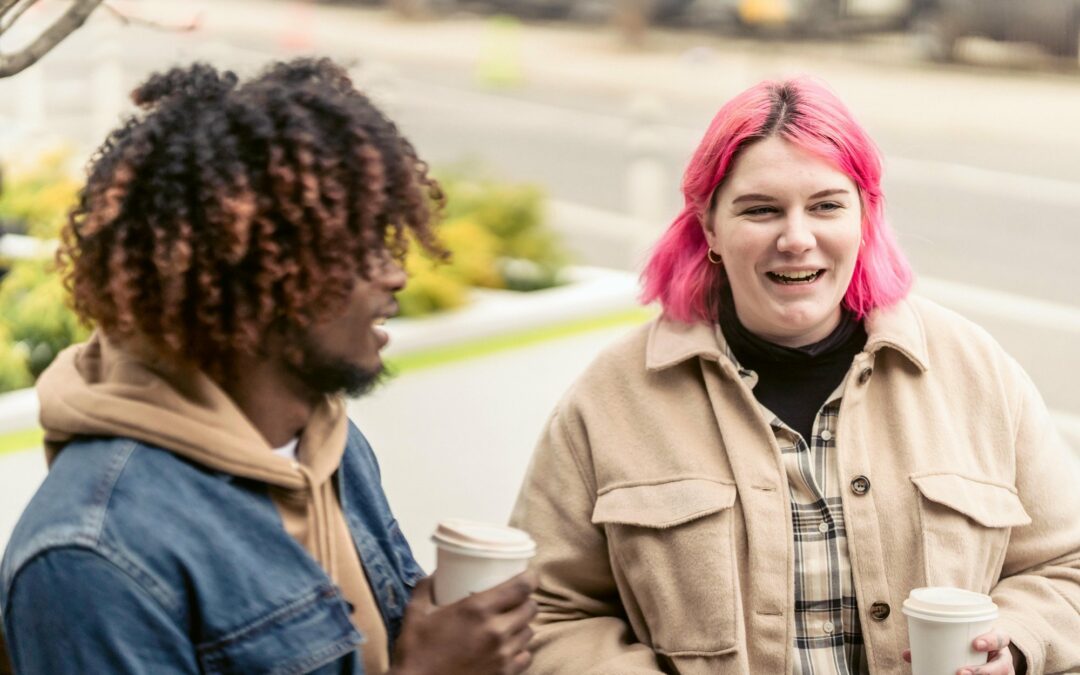 image of a two friends sharing a coffee one is a person with natural hair and the other has bright pink hair, they are both showing, illustrating Virtalent's commitment to being a Mindful Employer