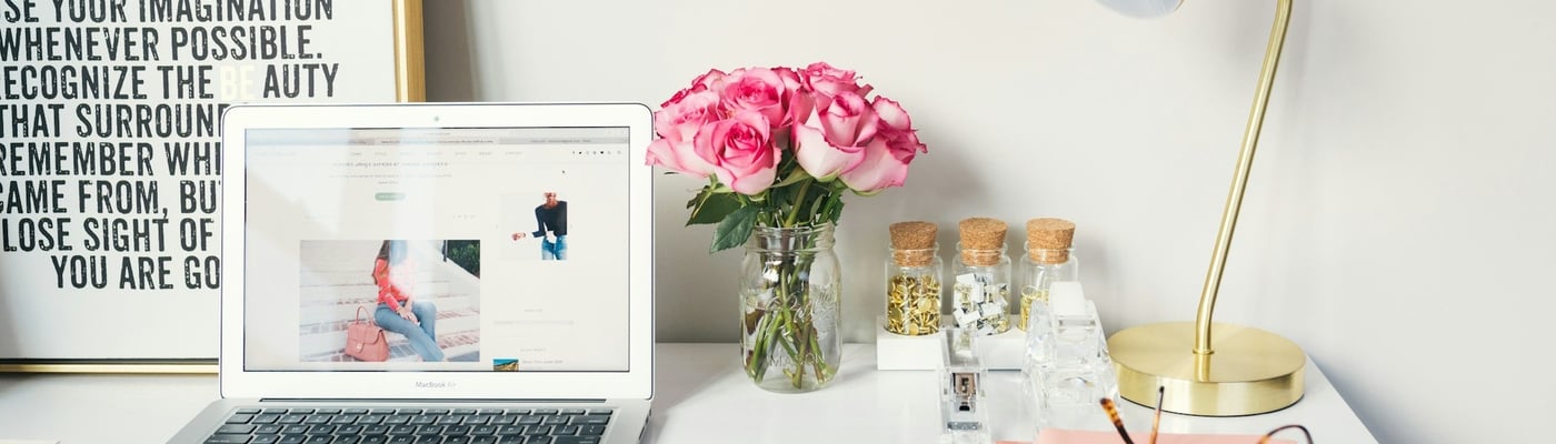 Image of a clean and tidy desk with lamp, laptop, phone, a print nad some roses