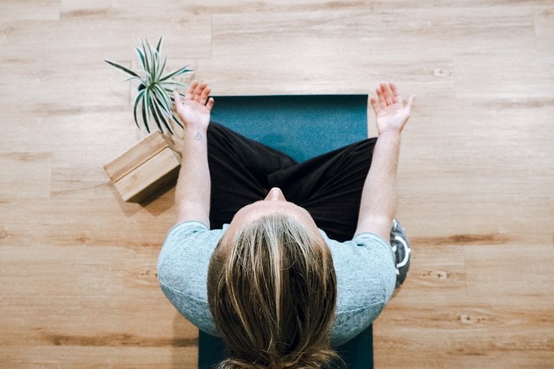 birdseye view of a woman sat on a yoga mat practicing meditation