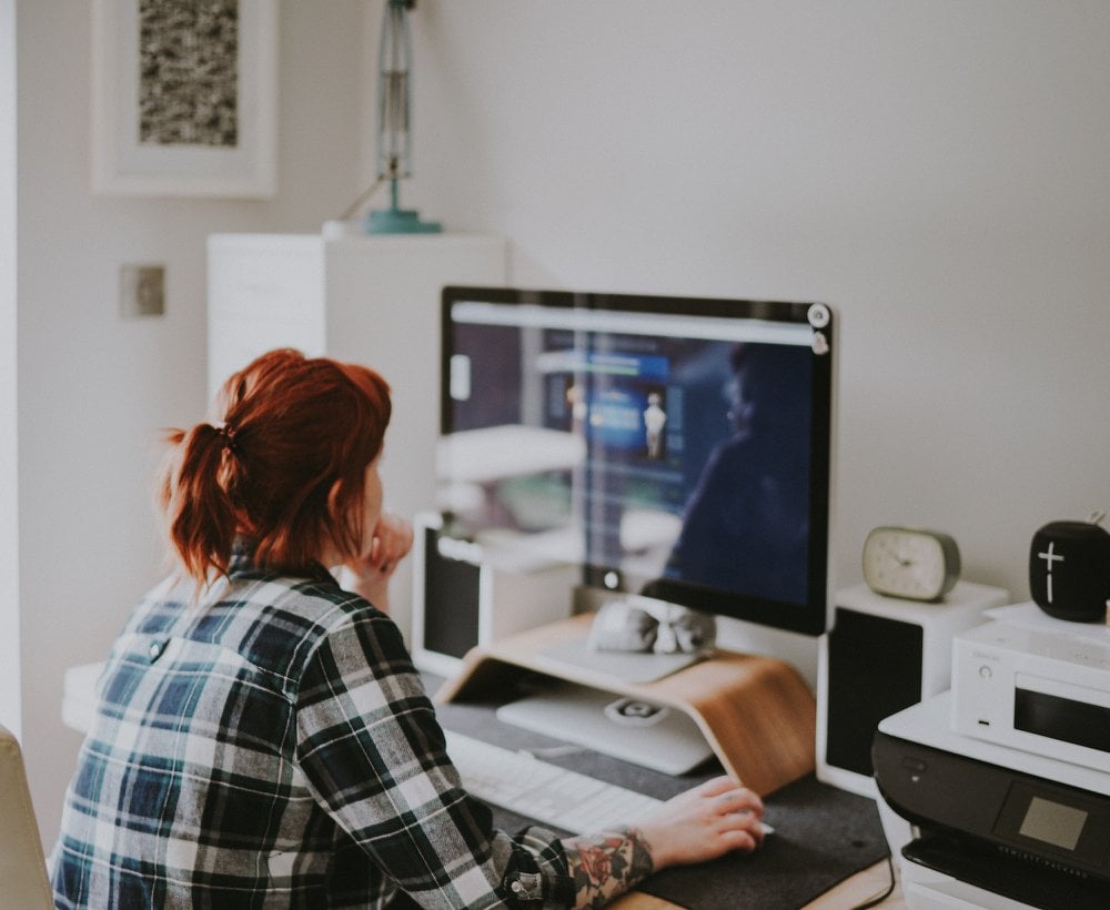 a woman with red hair and a ponytail who works as a virtual assistant is sat facing a computer at a desk